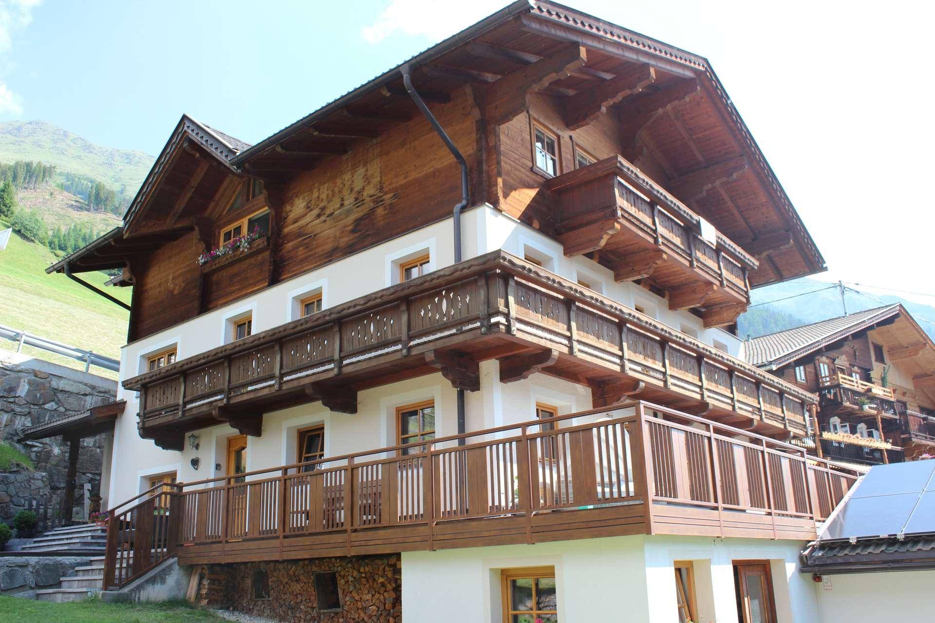 Traditionelles Holzhaus mit mehreren Balkonen und weißer Fassade, eingebettet in eine Berglandschaft.