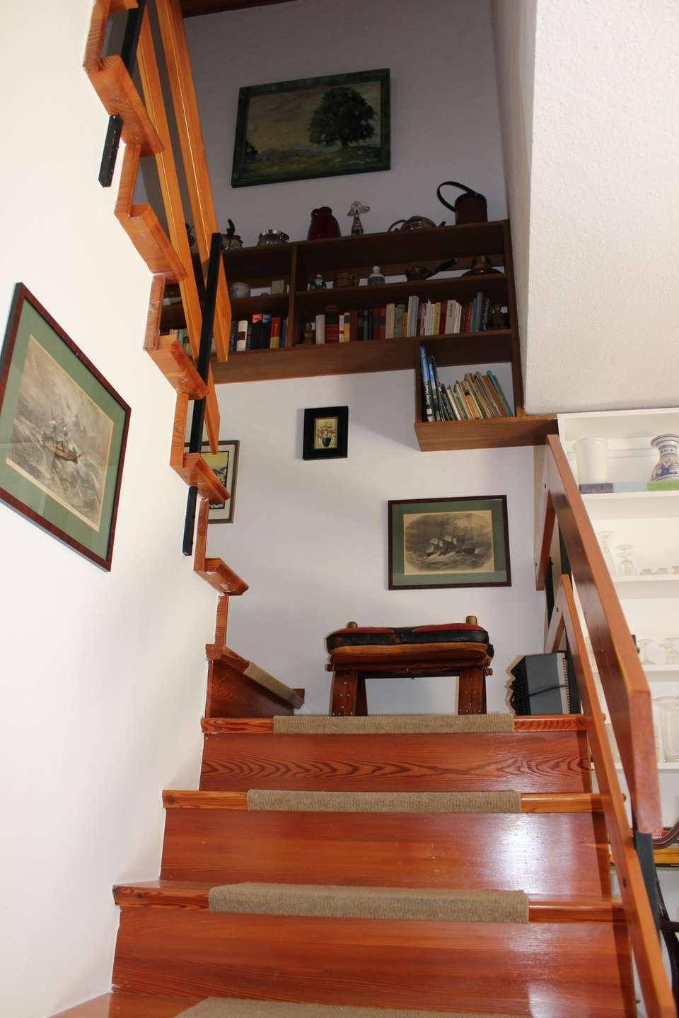 Holztreppe mit Teppichläufer und Wanddekorationen, die zu den oberen Etagen führt.
