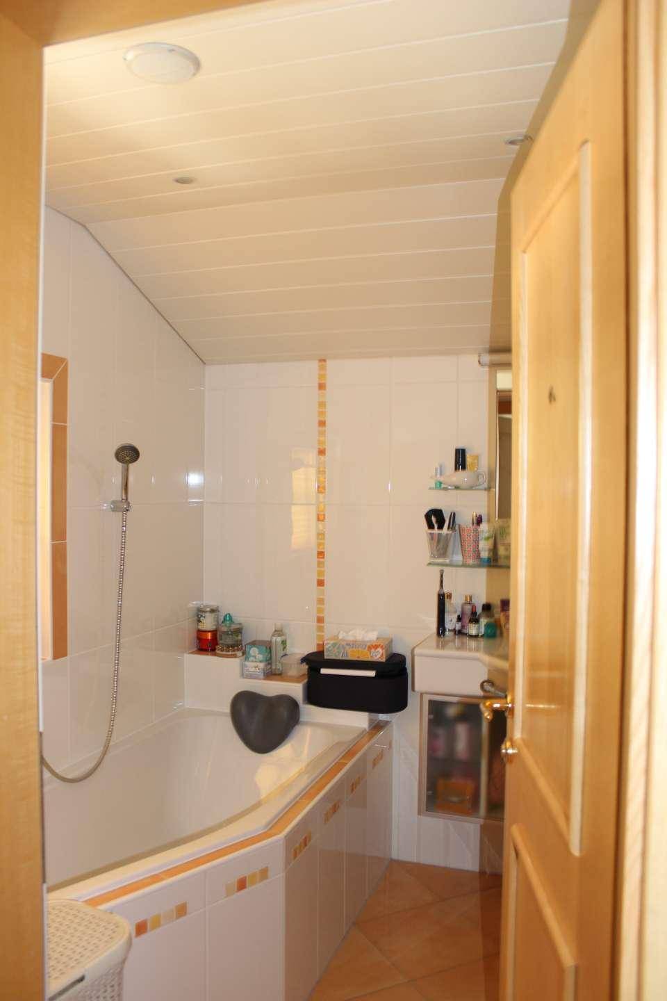 Badezimmer mit weißen Fliesen, Badewanne mit Duschfunktion und Dachschräge, gut beleuchtet.