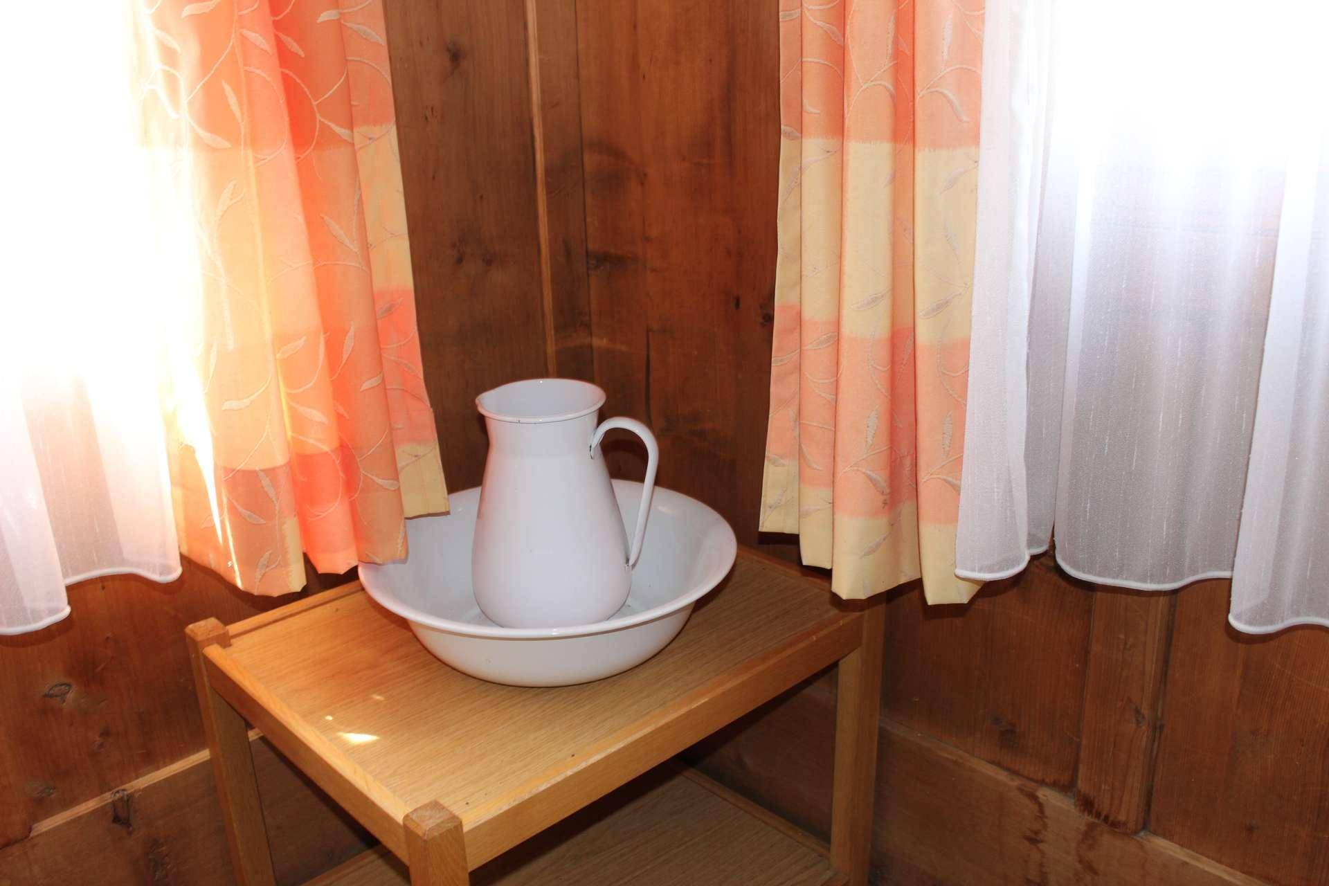 Ecke mit holzvertäfelten Wänden, einem Fenster mit Vorhängen und einem traditionellen Waschgeschirr.