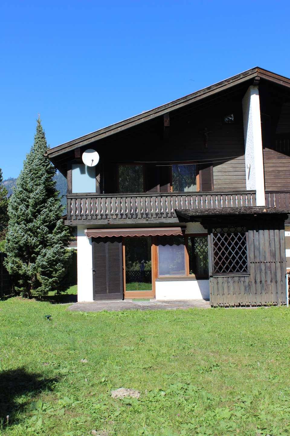 Nahaufnahme der Hausrückseite mit Balkon, Terrasse und gepflegtem Rasen unter blauem Himmel.