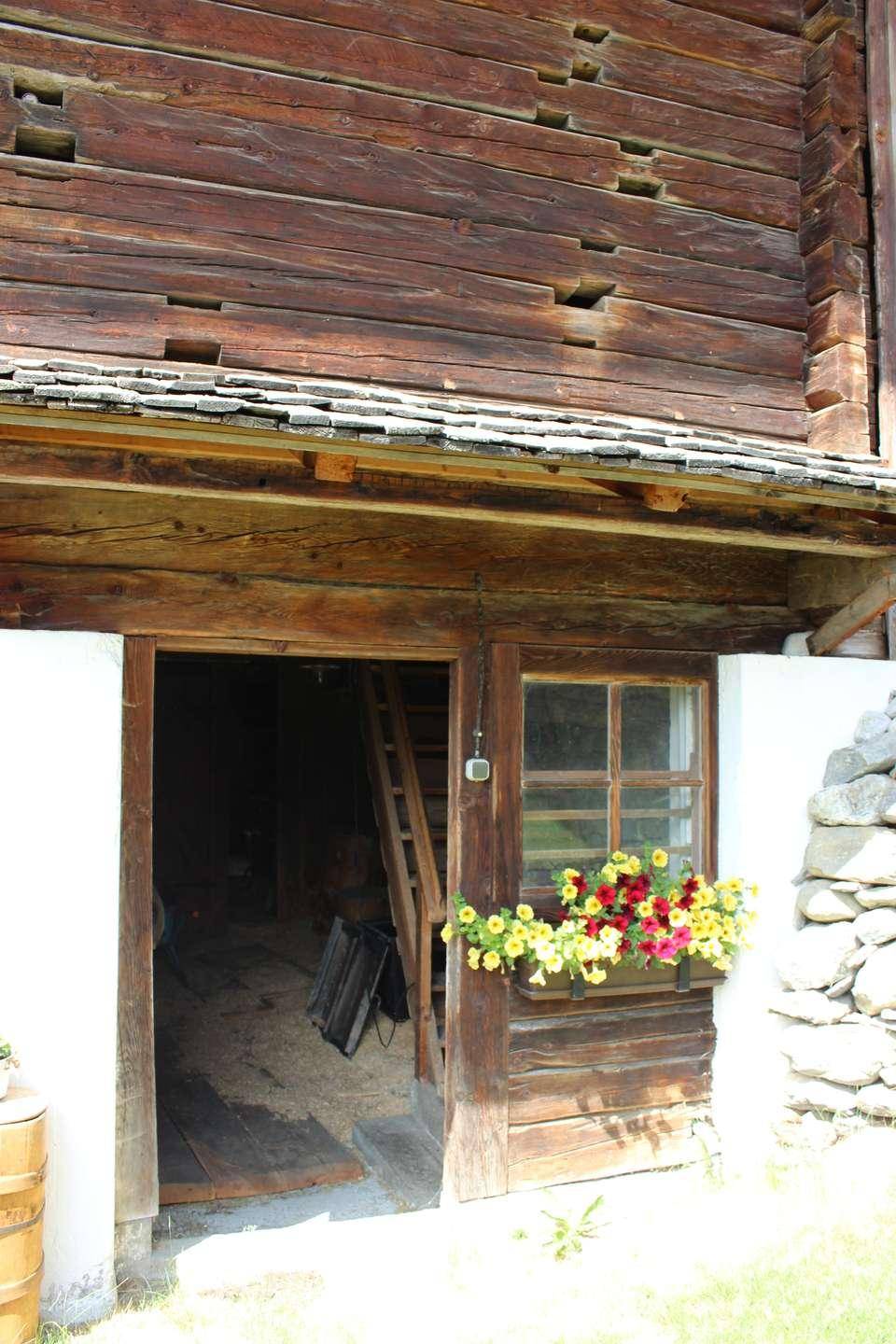Eingang zu einem rustikalen Holzgebäude mit Holztür und Fensterbank mit bunten Blumen.