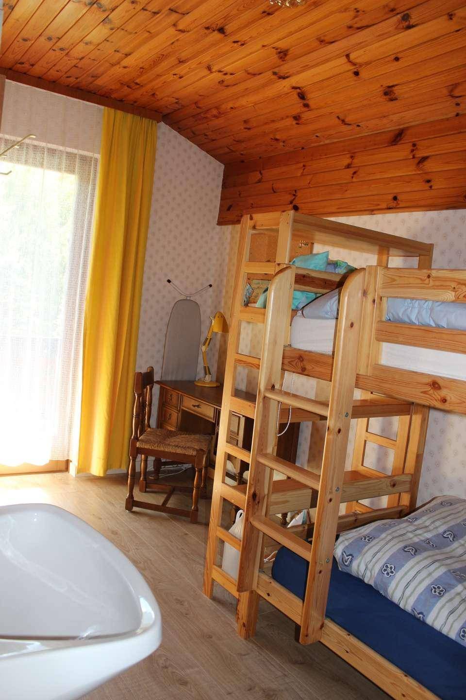 Kinderzimmer mit Etagenbetten, Holzbalkendecke und hellem Fenster mit gelben Vorhängen.