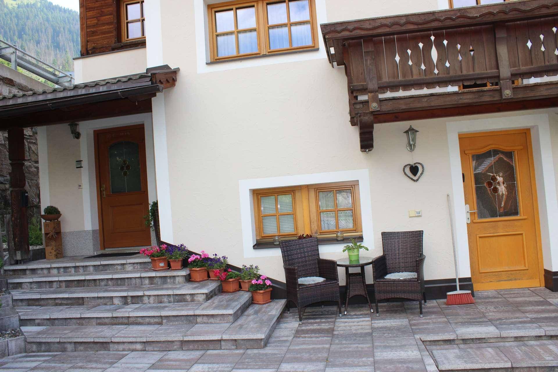 Eingangsbereich eines Hauses mit zwei Holztüren, Steinstufen und einer kleinen Sitzgelegenheit im Freien.
