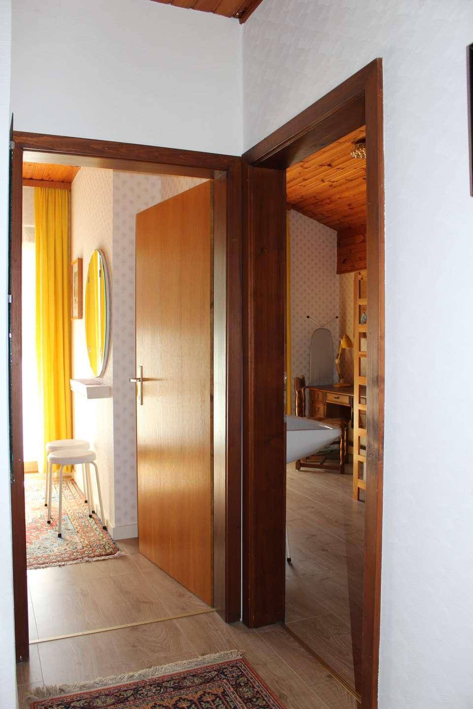 Flur mit Holztüren und Blick in angrenzende Zimmer mit gelben Vorhängen und Holzböden.