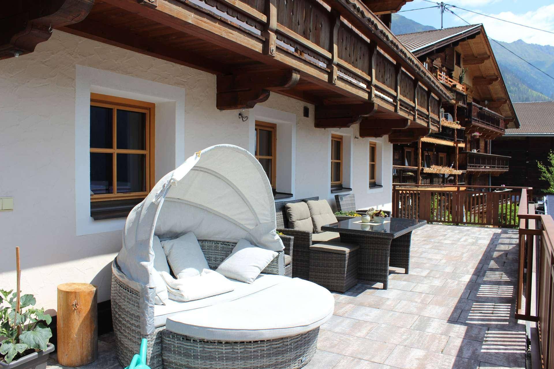 Große Außenterrasse mit modernen Rattanmöbeln und einem Tagesbett, mit Blick auf die Berge.