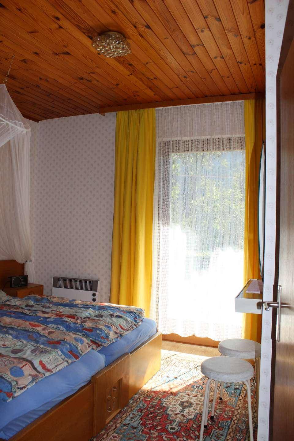 Helles Schlafzimmer mit Doppelbett, Holzbalkendecke und gelben Vorhängen am Fenster.
