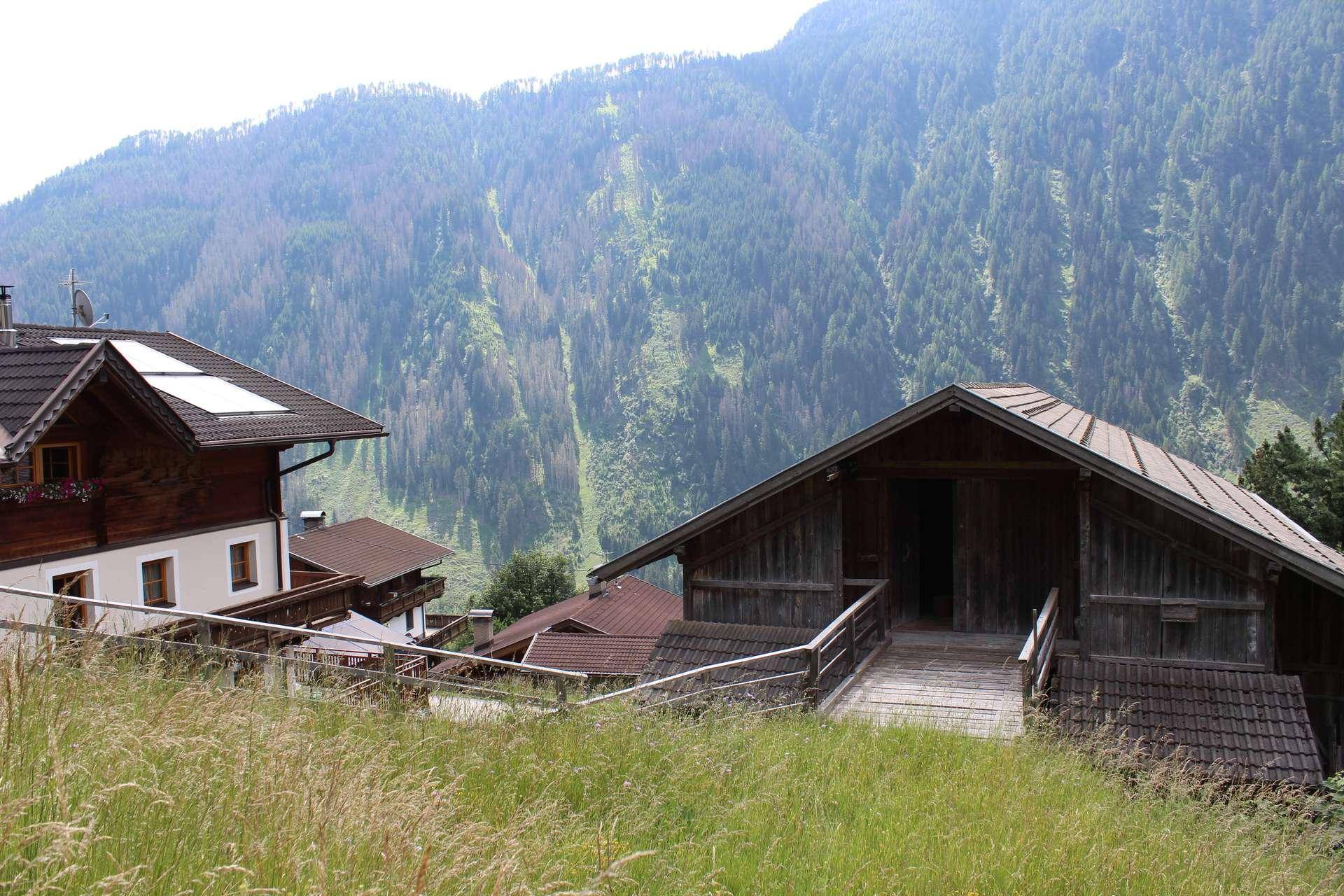Traditionelle Gebäude in den Bergen mit grünen Hängen und bewaldeter Landschaft im Hintergrund.