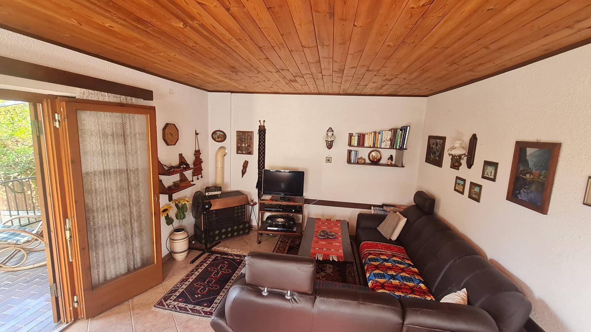 Gemütliches Wohnzimmer mit Holzbalkendecke, dunklem Sofa und traditioneller Dekoration.