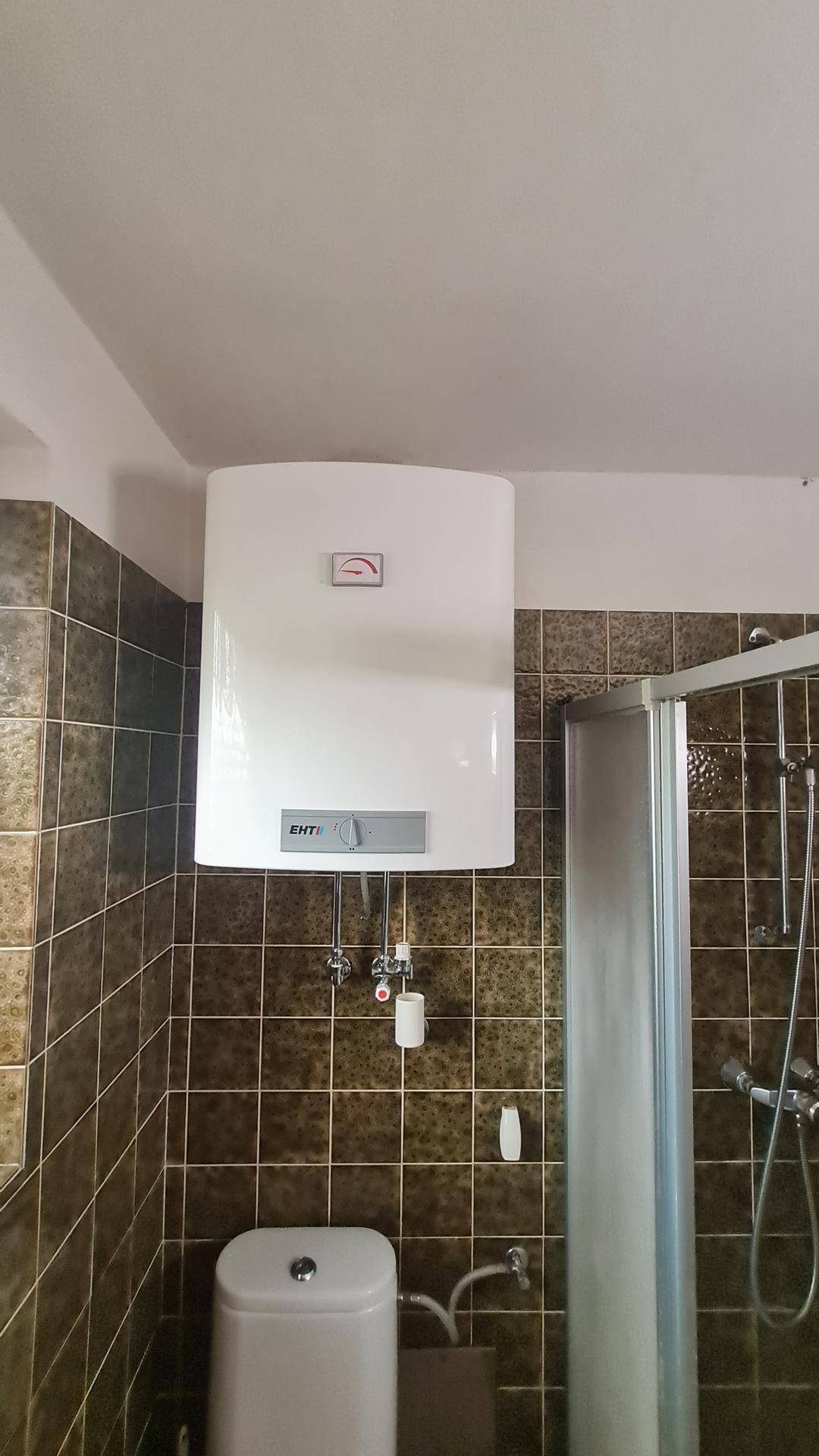 Detailansicht des Warmwasserboilers im Badezimmer über der Toilette.