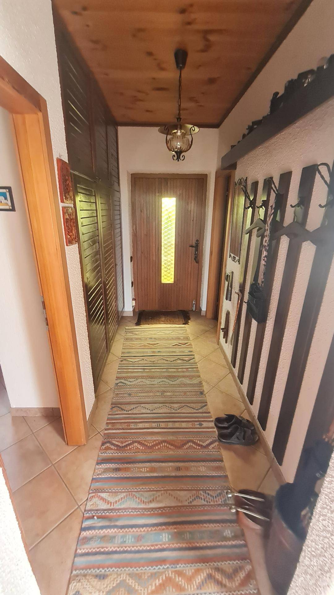 Heller Eingangsbereich mit gefliestem Boden, Holzdecke und Garderobe.