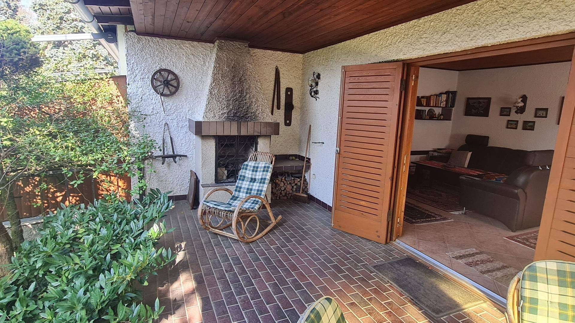 Überdachte Terrasse mit rustikalem Kamin, gefliestem Boden und Schaukelstuhl für entspannte Stunden.