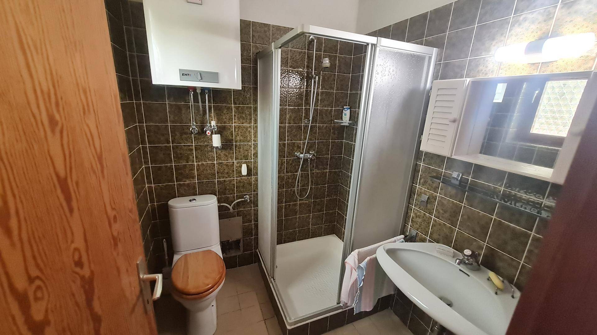 Badezimmer mit Dusche, WC und braunen Fliesen, ausgestattet mit einem Warmwasserboiler.