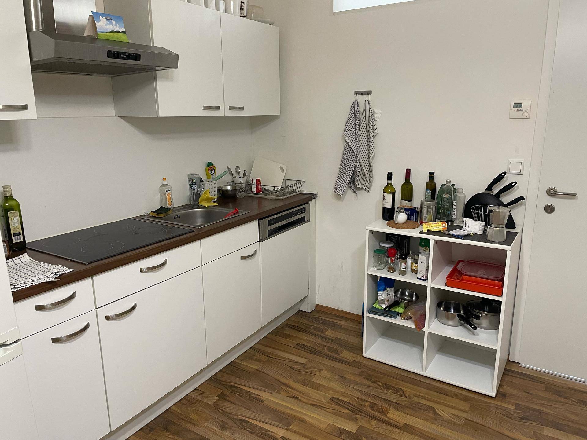 Funktionale Einbauküche mit weißen Schränken, Induktionskochfeld, Geschirrspüler und Dunstabzugshaube.