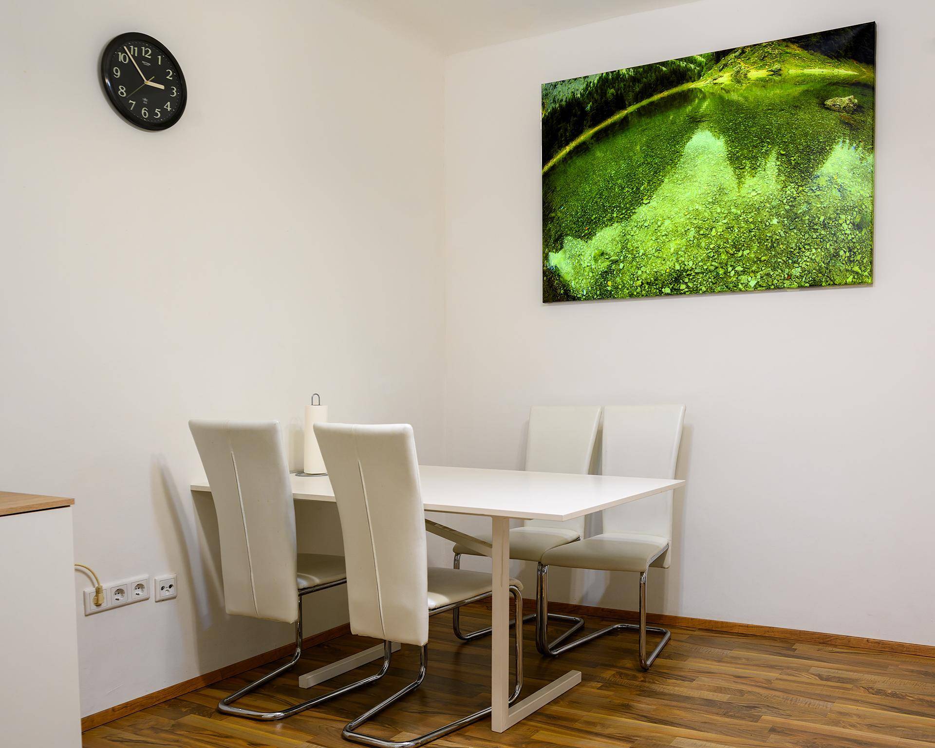 Moderner Essbereich mit weißem Tisch und vier Stühlen, akzentuiert durch ein großes grünes Kunstwerk.