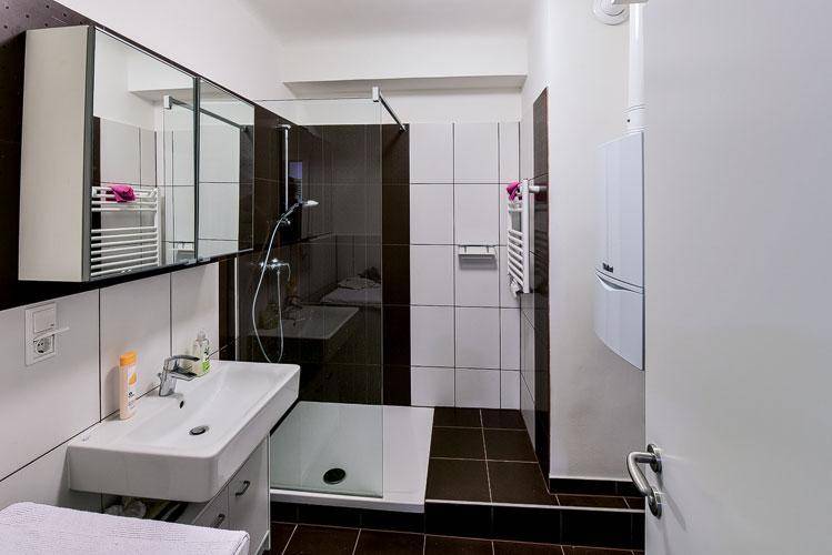 Modernes Badezimmer mit ebenerdiger Dusche, Waschbecken, Spiegelschrank und beheiztem Handtuchhalter.