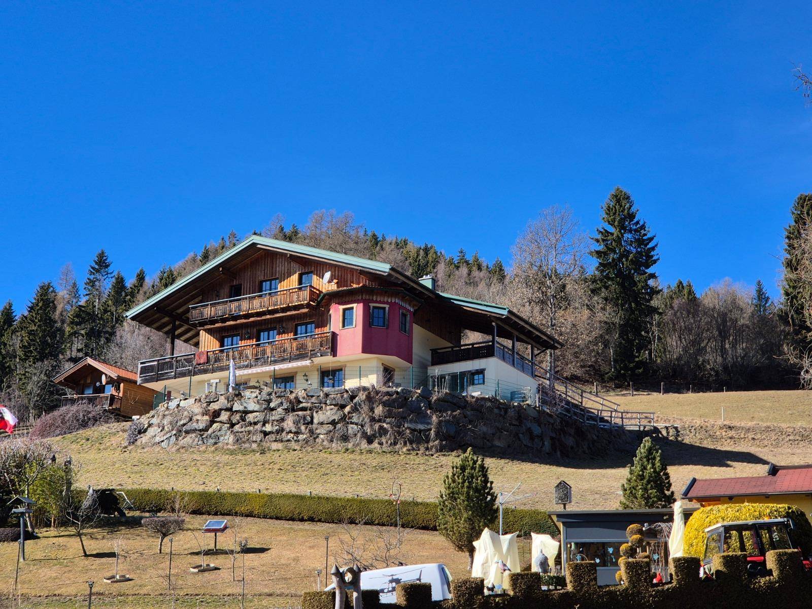 Großes Holzhaus auf einem Hügel mit mehreren Balkonen und weitem Blick.