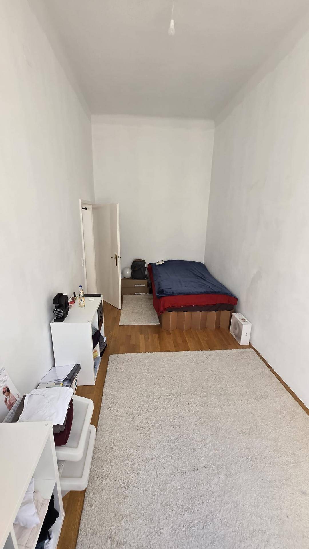 Schmales Schlafzimmer mit Holzboden, Teppich und einfacher Einrichtung.