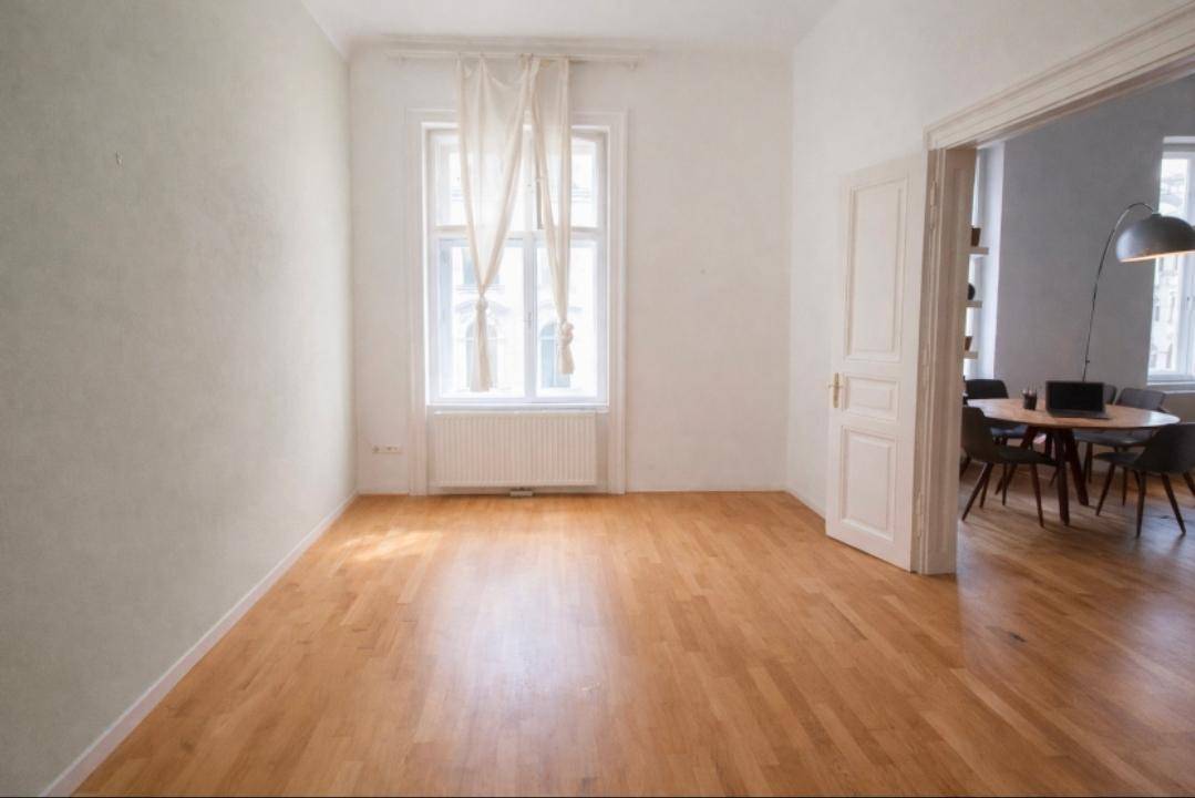 Heller Raum mit Parkettboden und hohen Decken, offen zu einem Essbereich.