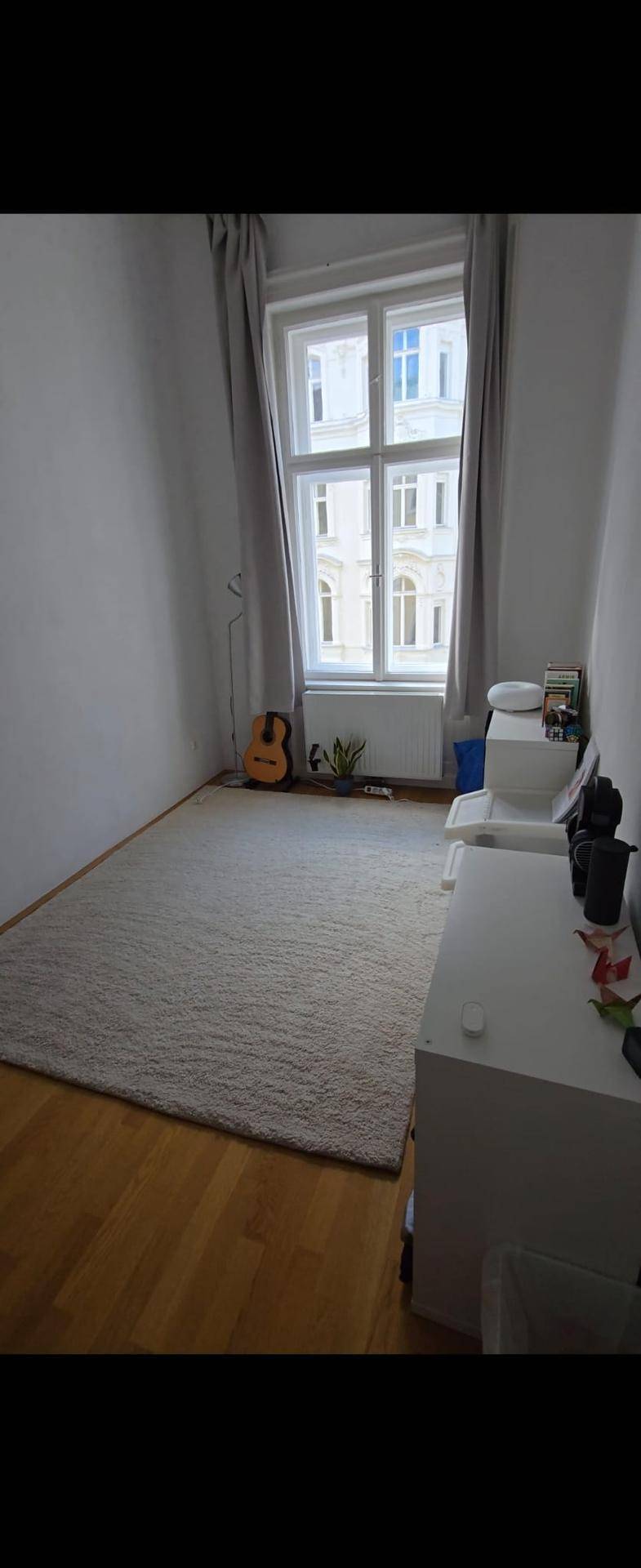 Helles Schlafzimmer mit Holzboden, großem Fenster und beigem Teppich.