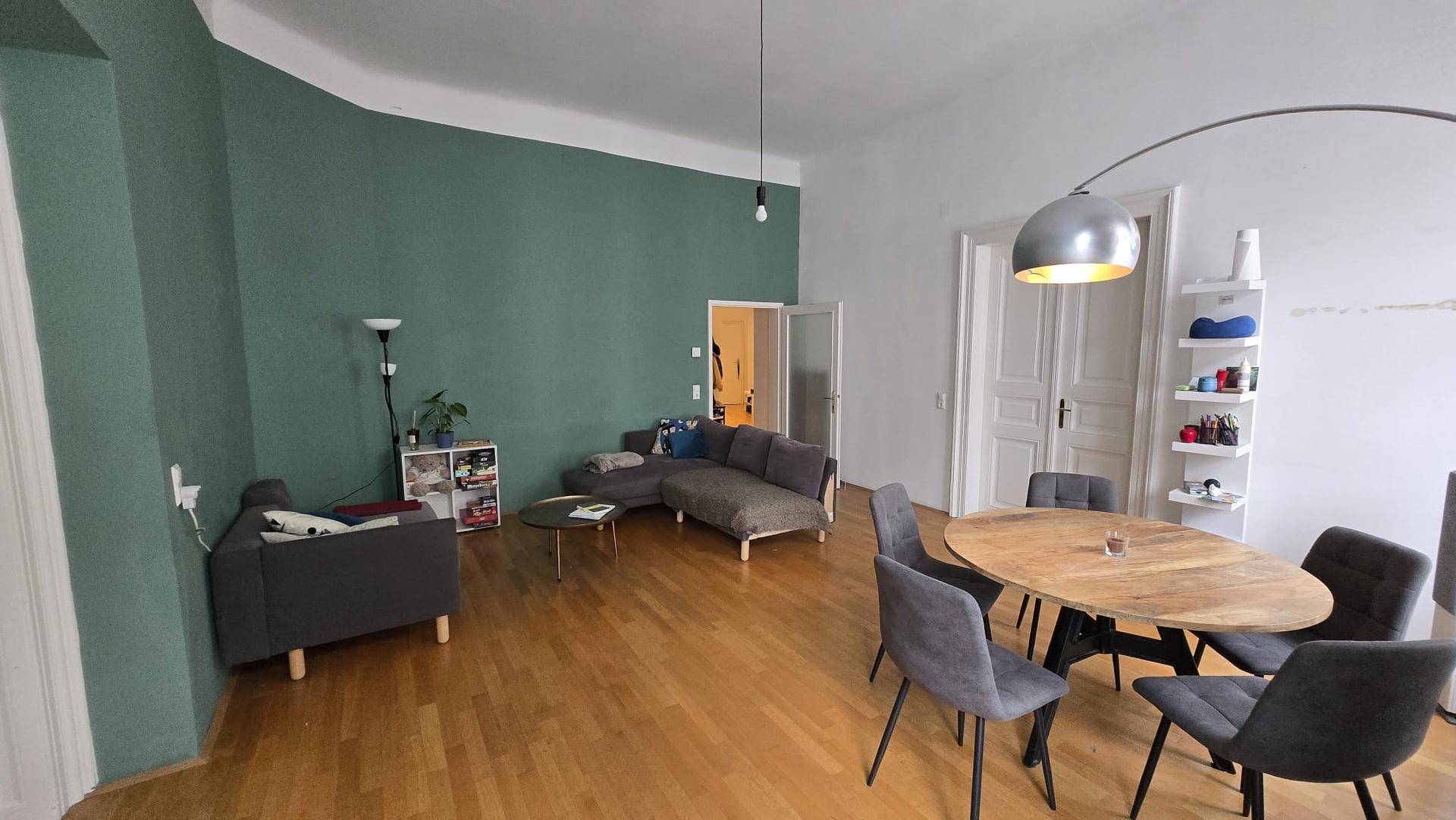 Heller Wohn-Essbereich mit Parkettboden, moderner Einrichtung und grüner Wand.
