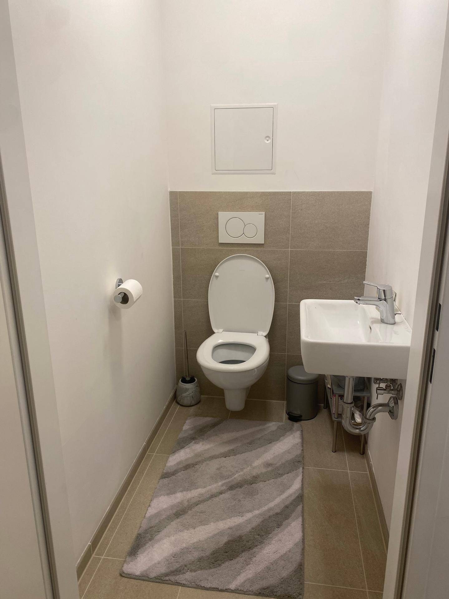 Helles Gäste-WC mit Wand-WC, kleinem Waschbecken und modernen Fliesen an Wand und Boden.
