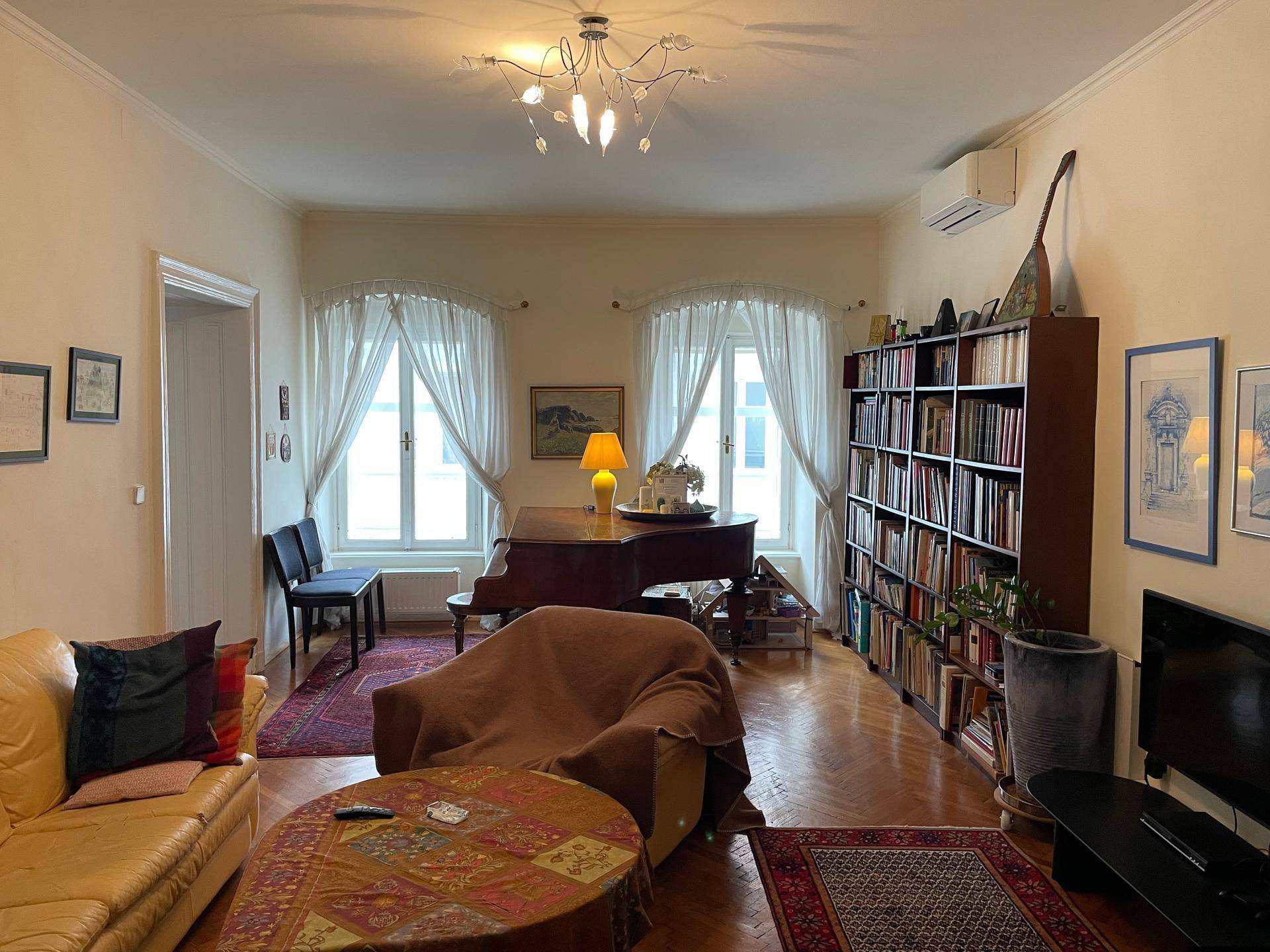 Gemütliches Wohnzimmer mit Parkettboden, Klavier und Bücherregalen, ideal zum Entspannen.