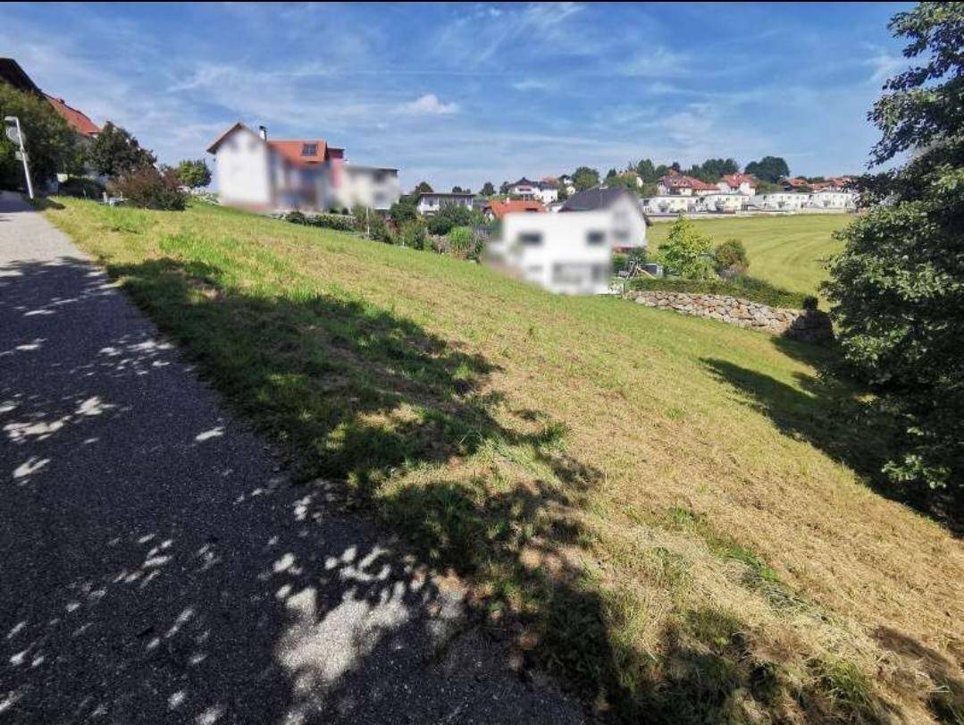 Grüner Hang mit Blick auf eine Wohnsiedlung und weitere Hügel in der Ferne.