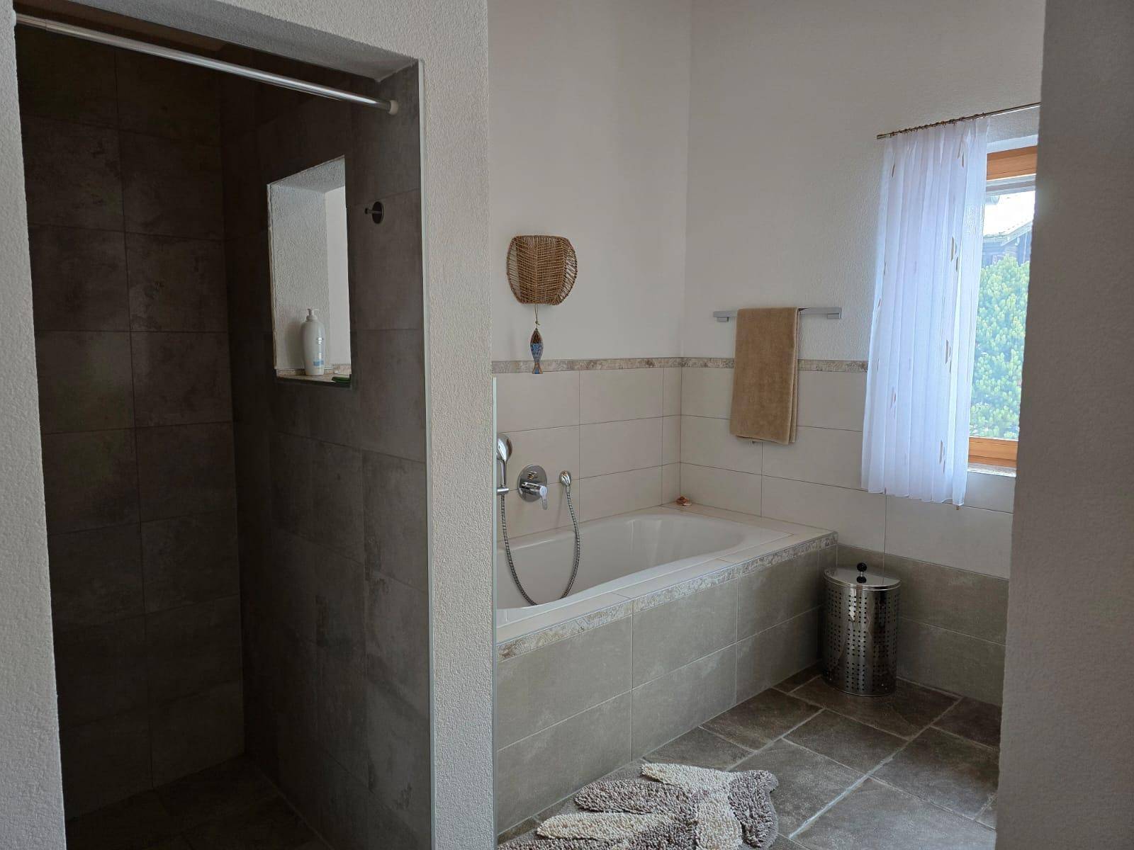 Badezimmer mit Badewanne, Duschbereich und Fliesenboden in neutralen Farbtönen.