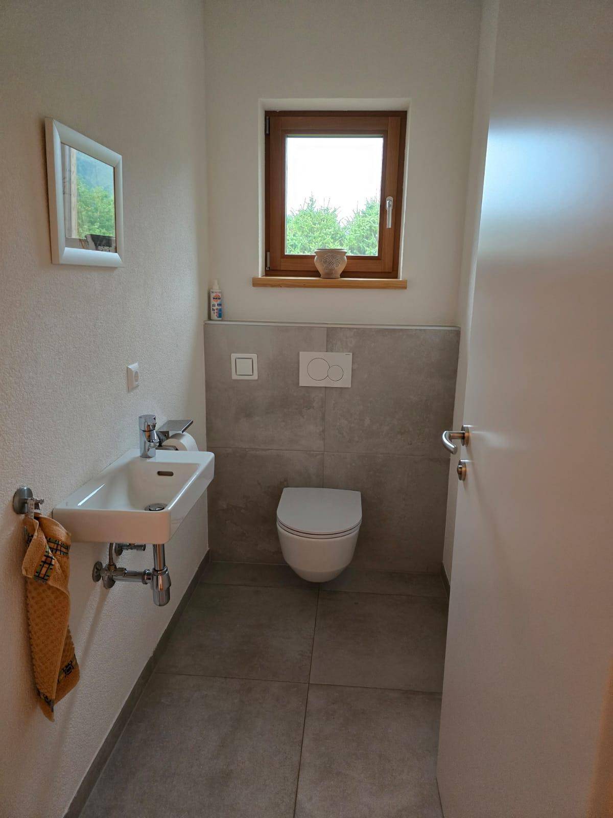 Modernes Gäste-WC mit wandhängendem WC, kleinem Waschbecken und Fenster.