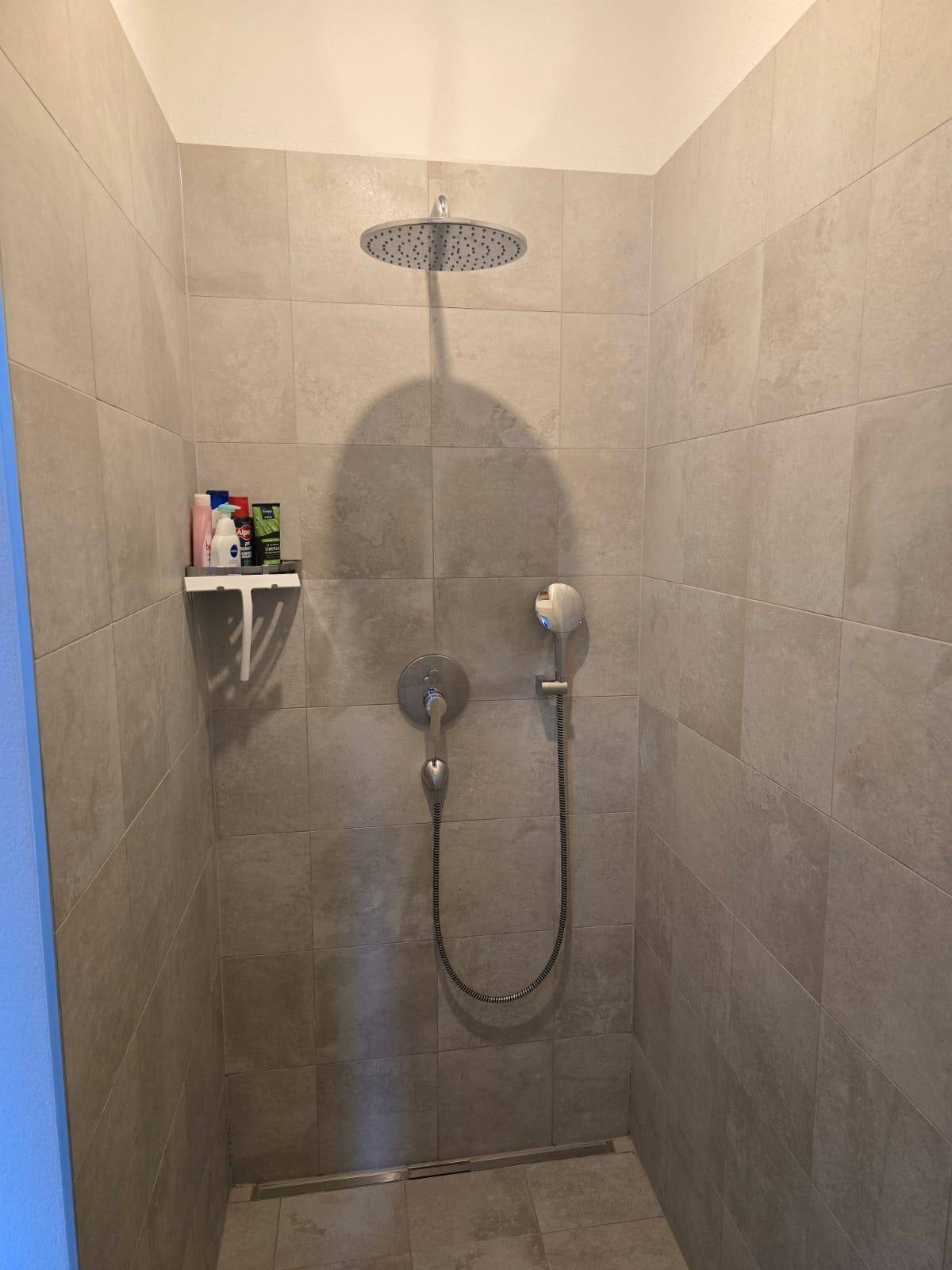 Moderne begehbare Dusche mit Regenduschkopf und großformatigen Fliesen.