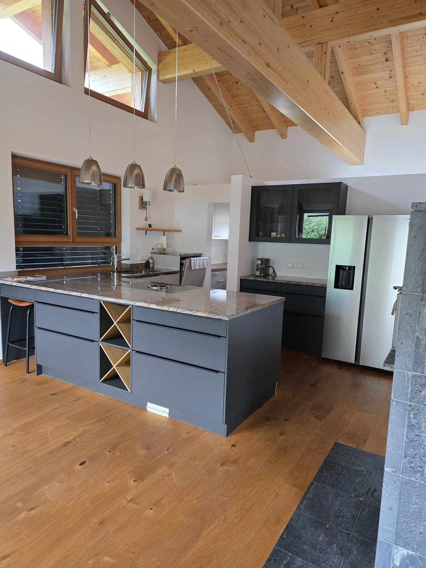 Moderne offene Küche mit Kücheninsel, Granitarbeitsplatte und Holzbalkendecke.