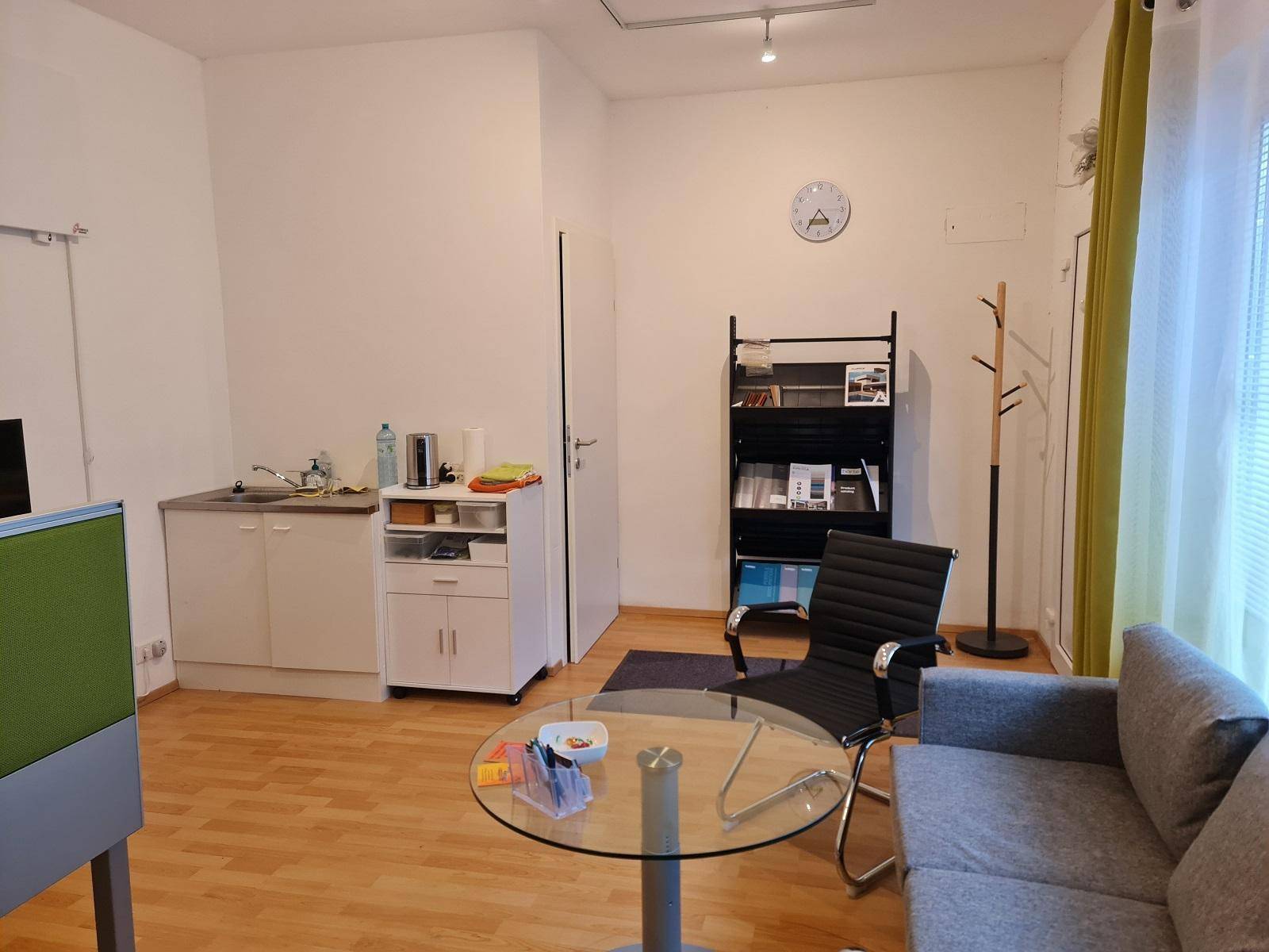 Heller Wohn- und Bürobereich mit kleiner Küchenzeile, Sofa und Holzboden.