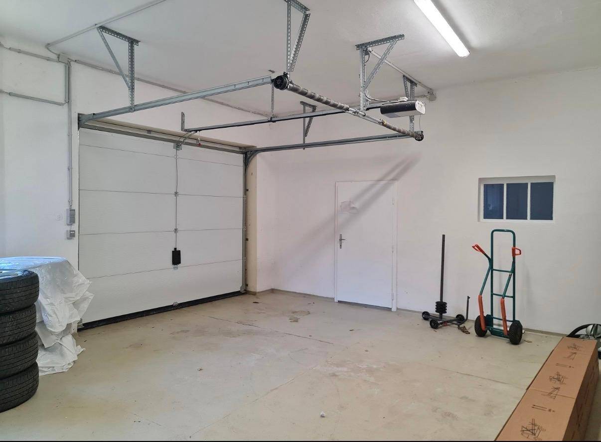 Geräumige Garage mit Rolltor, kleinem Fenster und Betonboden, ideal für Fahrzeuge oder Lagerung.