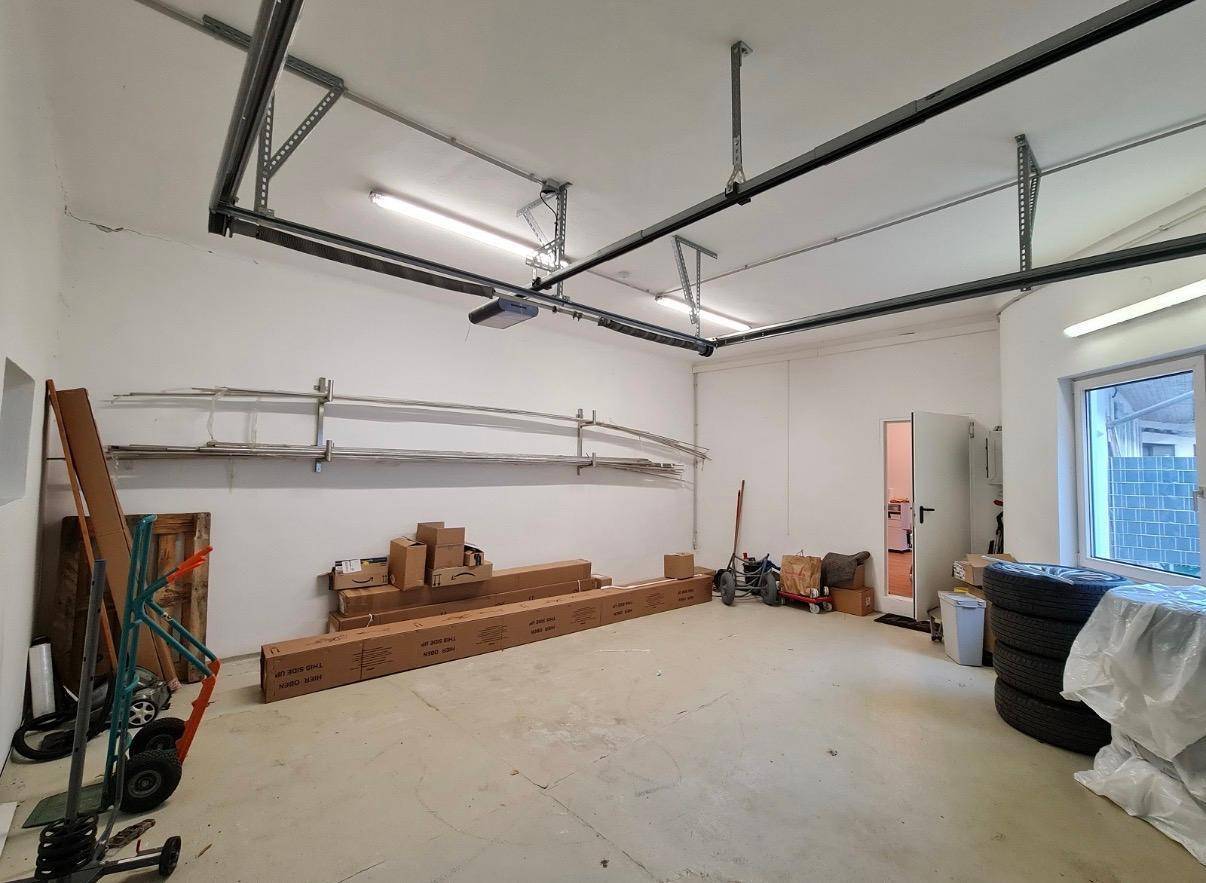 Große Garage mit viel Stauraum, Betonboden und einem Fenster, das Tageslicht hereinlässt.