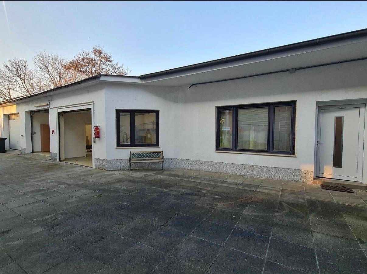 Außenansicht des Gebäudes mit Garagentoren, Fenstern und einem gepflasterten Zugangsbereich.