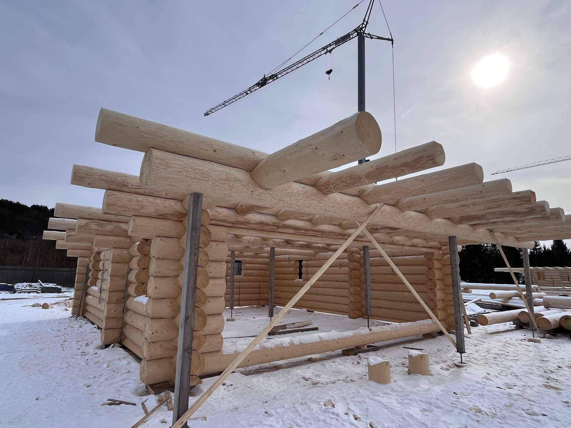 Blockhaus im Bau mit sichtbaren Holzstämmen und Dachkonstruktion unter winterlichem Himmel.