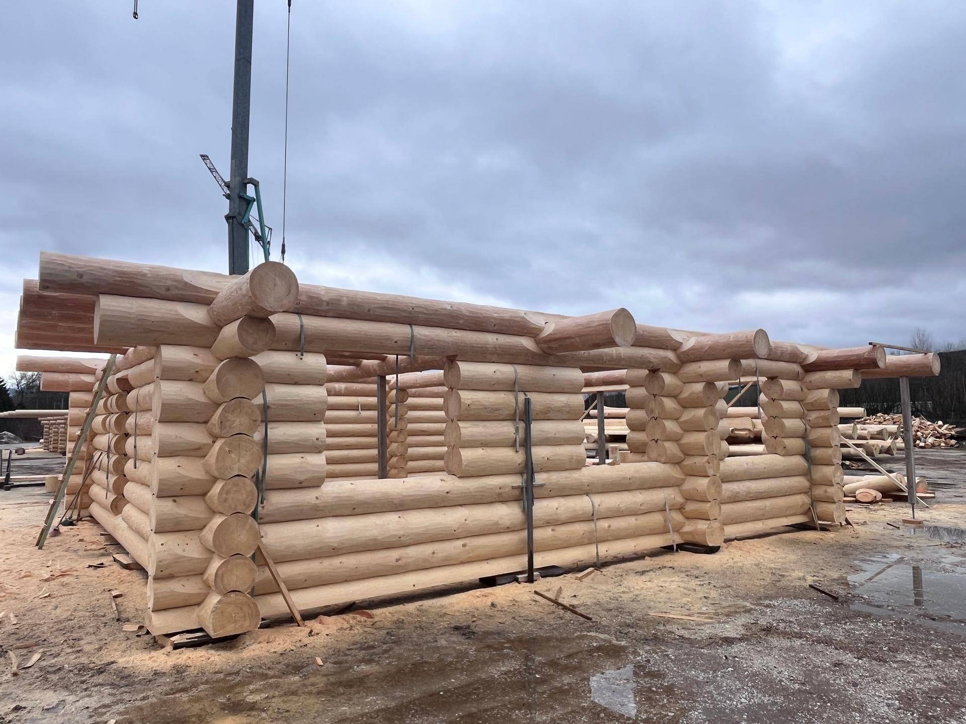 Rohbau eines Blockhauses aus Holzstämmen auf einer Baustelle unter bewölktem Himmel.