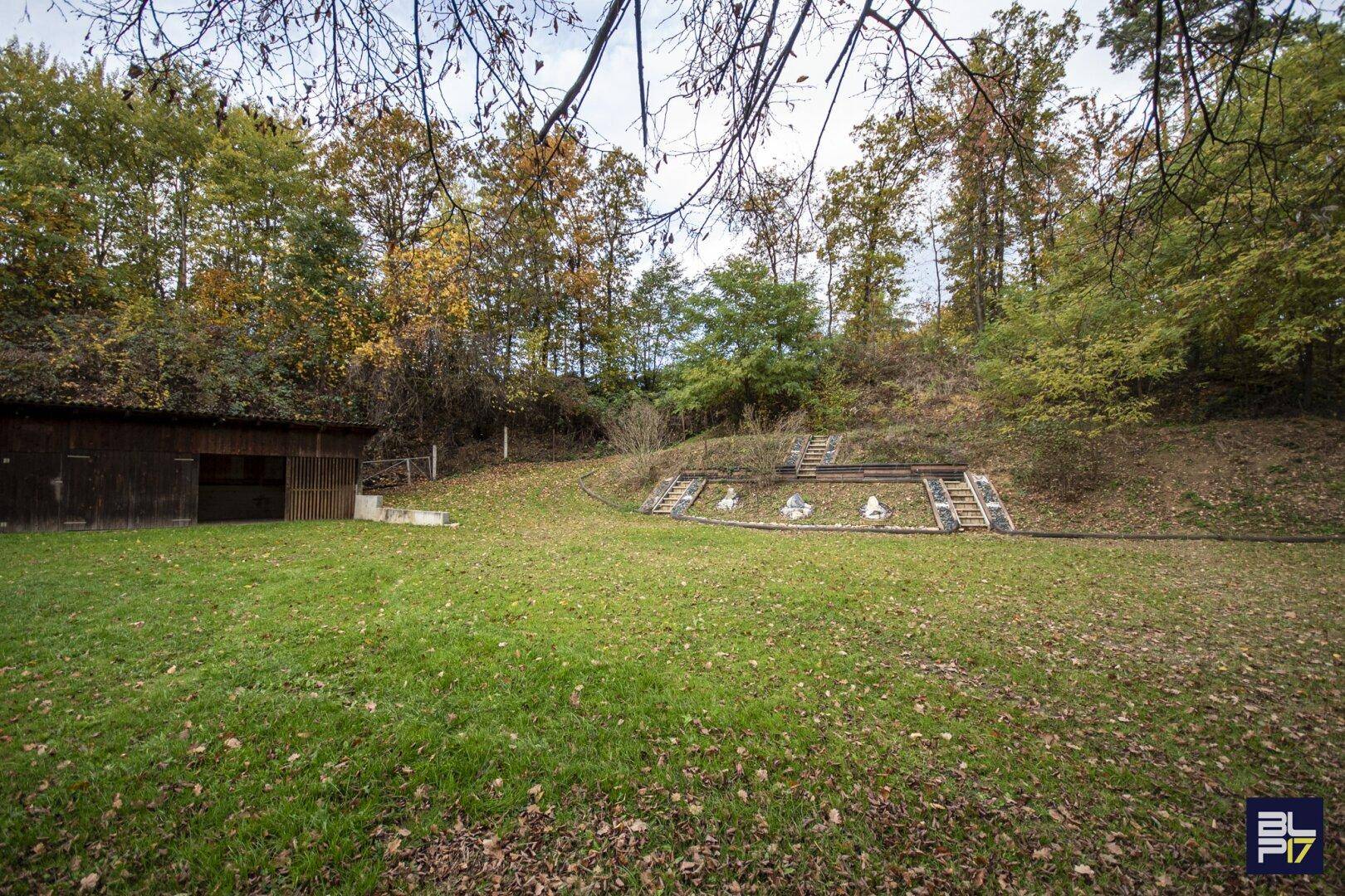 Großer Gartenbereich mit Rasenfläche, Bäumen und einer Holzhütte im Hintergrund.