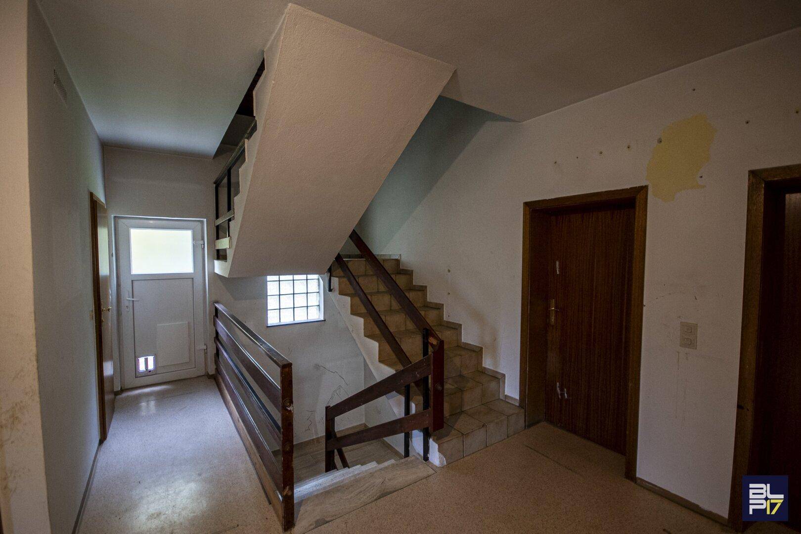 Treppenhaus mit Holzgeländer und Fliesenboden, das die verschiedenen Etagen verbindet.