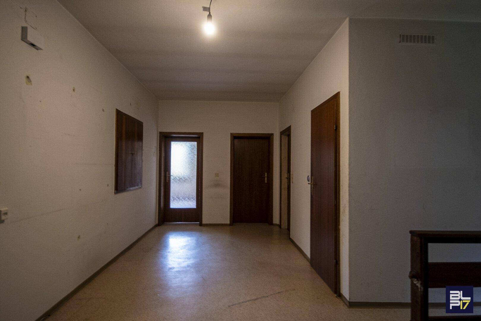 Langer Flur mit Terrazzoboden und mehreren Türen, der zu verschiedenen Räumen führt.