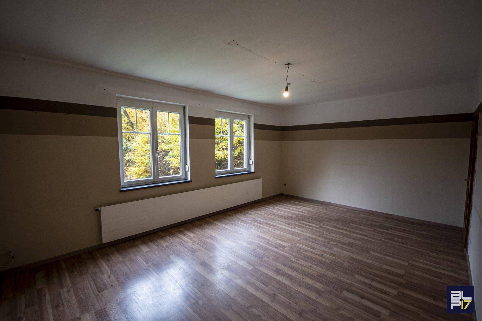 Geräumiges Wohnzimmer mit Laminatboden und großen Fenstern mit Blick ins Grüne.