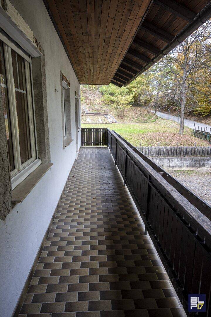 Langer Balkon mit Fliesenboden und Holzgeländer, der einen Blick ins Grüne bietet.