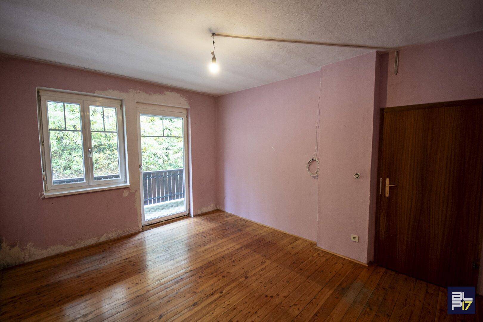 Schlafzimmer mit Holzdielenboden und Zugang zu einem Balkon mit Blick ins Grüne.