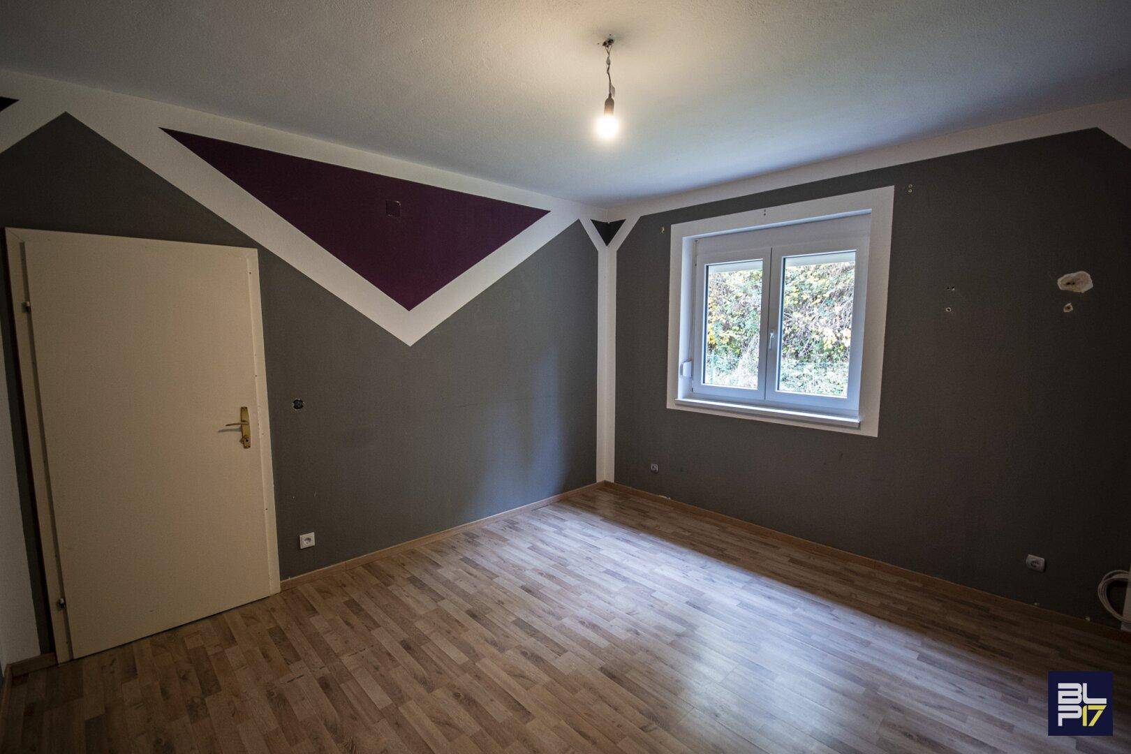 Schlafzimmer mit Laminatboden und kreativer Wandgestaltung in Grau und Lila.