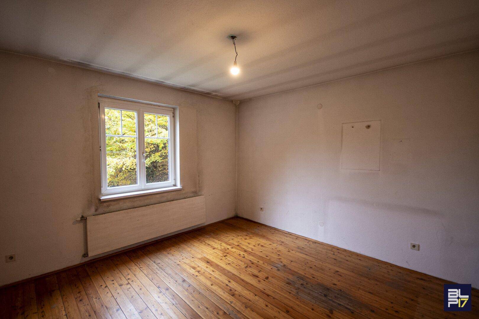 Helles Schlafzimmer mit Holzdielenboden und Fenster mit Blick auf die umliegende Natur.