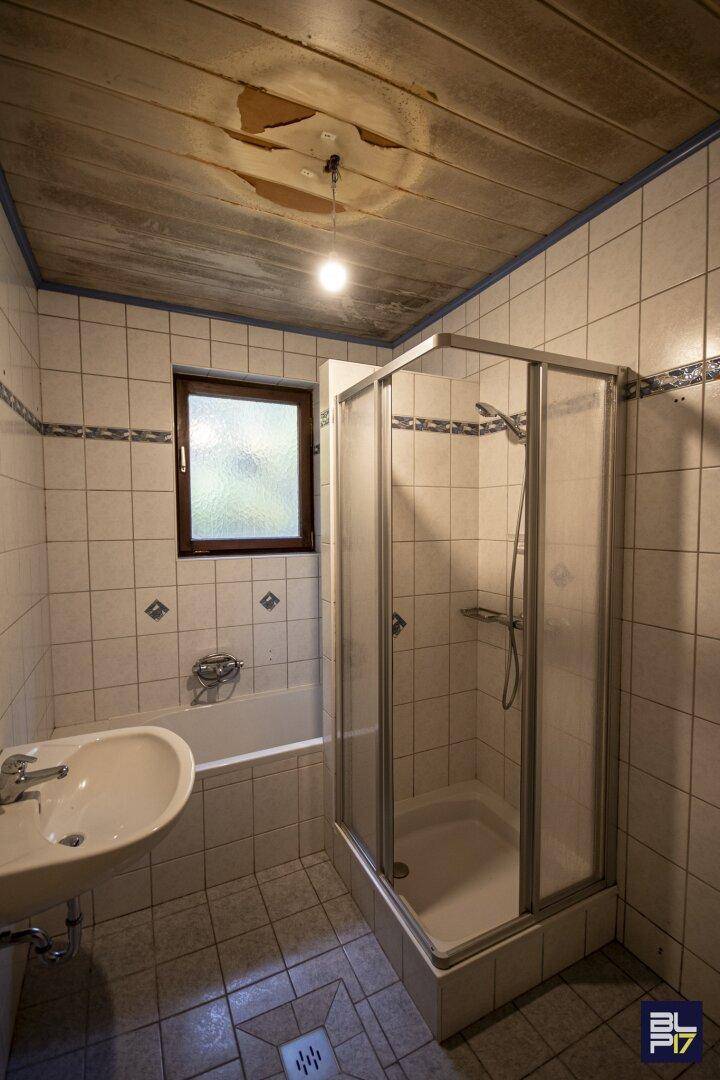 Gefliestes Badezimmer mit Badewanne, Duschkabine und Fenster, das renovierungsbedürftig ist.