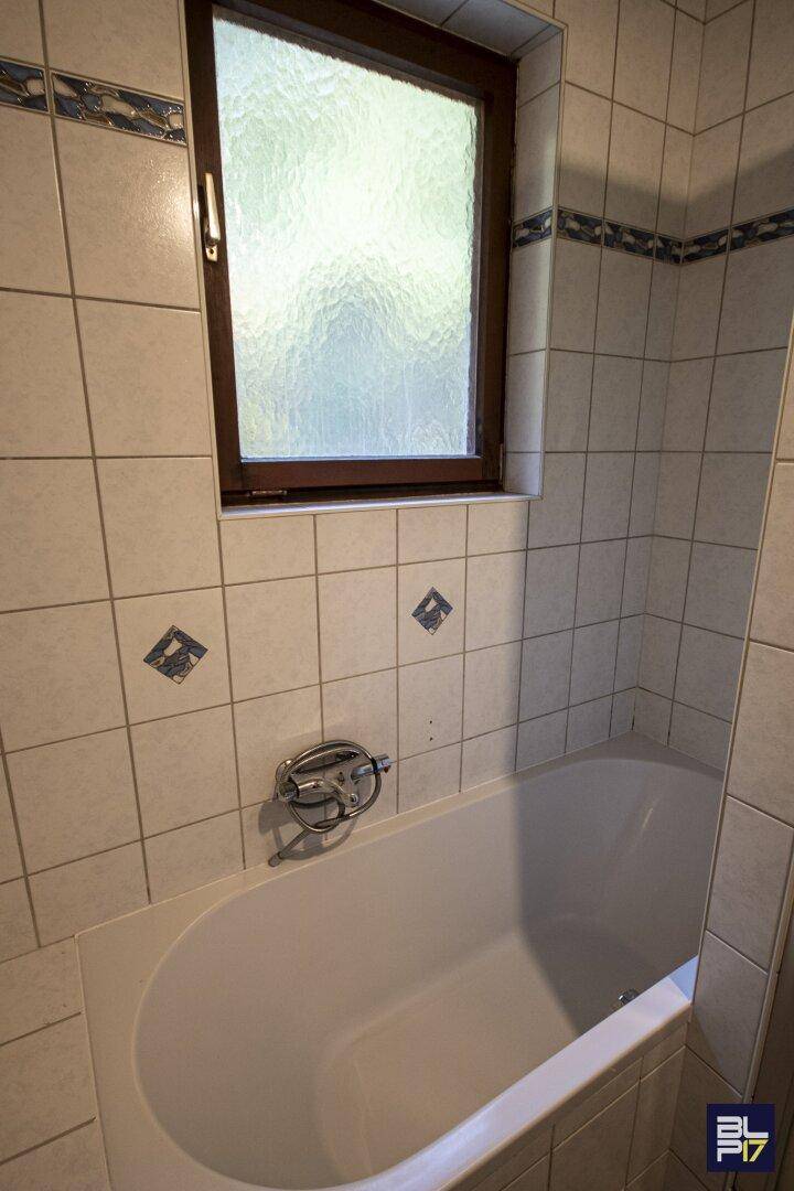 Detailansicht einer Badewanne in einem gefliesten Badezimmer mit Fenster.