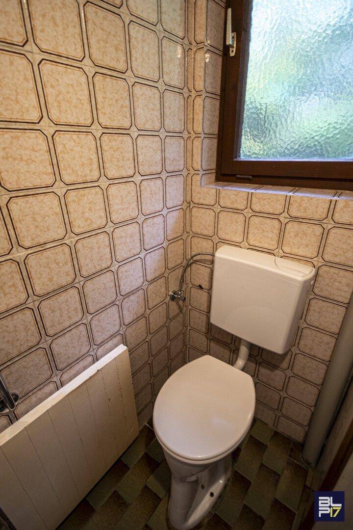 Separate Toilette mit gemusterten Fliesen an Wänden und Boden sowie einem Fenster.