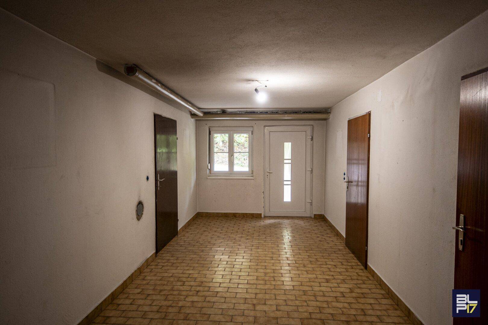 Kellerraum mit Fliesenboden, mehreren Türen und Fenstern, der als Abstellraum dient.